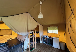 Interior de una tienda safari en Camping De La Vallée, Bélgica, con cama, cocina y área de descanso.