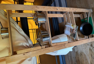 Interior de tienda safari en Camping De La Vallée, Bélgica, con escalera de madera, ollas y folleto.