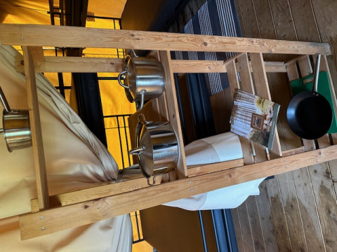 Interior de tienda safari en Camping De La Vallée, Bélgica, con escalera de madera, ollas y folleto.