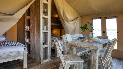 Vista interior de una tienda safari de lujo con muebles de madera, comedor y camas acogedoras, Safari tent Mill.