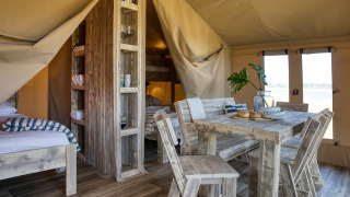 Indretning af en luksuriøs safaritelt med træmøbler, spisebord og hyggelige senge hos Safari tent Mill.