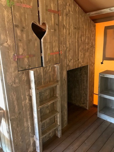 Interieur van een safaritent met houten ladder en een deur met hartvorm bij Camping Sevink Molen, Nederland.