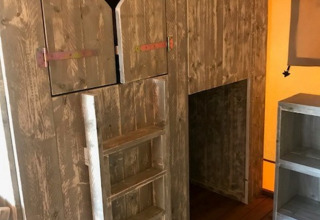 Interno di tenda safari con scala di legno e porta con intaglio a cuore presso Camping Sevink Molen, Paesi Bassi.