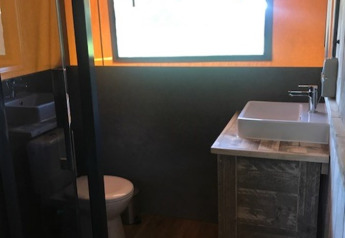 Modern bathroom in Safari tent Hilgelo at Camping Sevink Molen, Netherlands, featuring wood accents and window.