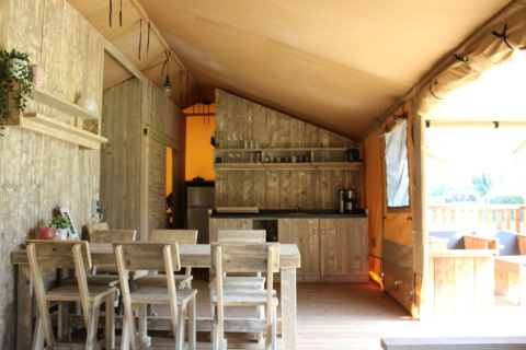 Vista interior de la tienda Safari Hilgelo en Camping Sevink Molen, con muebles rústicos de madera y cocina.