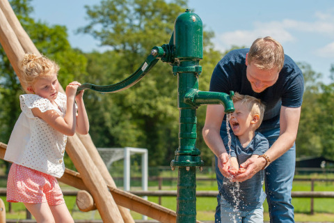 Un uomo aiuta due bambini a pompare acqua da una pompa verde al Camping Sevink Molen, Gelderland, Paesi Bassi.