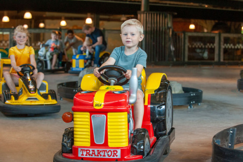 Niños conducen pequeños tractores eléctricos en una pista interior en Camping Sevink Molen, Gelderland, Países Bajos.