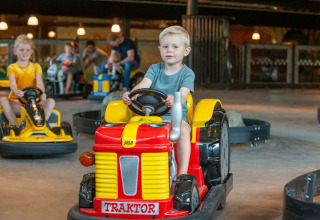 Children ride small electric tractors in an indoor track at Camping Sevink Molen holiday park, Gelderland, Netherlands.