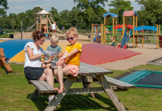 Moeder en twee kinderen op houten bank bij speeltuin, Camping Sevink Molen, Gelderland, Nederland.