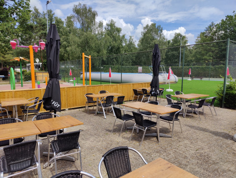 Zona de asientos al aire libre en Camping Het Veen, Amberes, con parque infantil y campo verde al fondo.