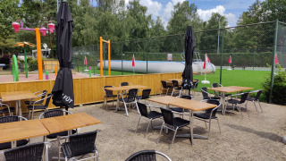 Zona de asientos al aire libre en Camping Het Veen, Amberes, con parque infantil y campo verde al fondo.