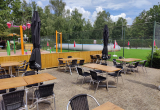 Zona de asientos al aire libre en Camping Het Veen, Amberes, con parque infantil y campo verde al fondo.