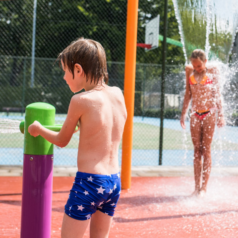 Kinder spielen an einem Wasserspielplatz im Sonnenschein im Ferienpark Camping Het Veen, Antwerpen, Belgien.