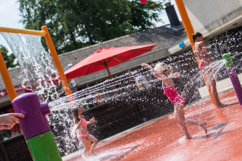 Kinder spielen in einem bunten Wasserspielplatz im Camping Het Veen, Antwerpen, Belgien, an einem sonnigen Tag.