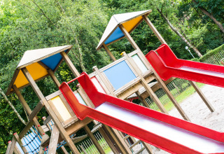 Bunter Spielplatz mit roten Rutschen und Holzhäusern bei Camping Het Veen in Antwerpen, Belgien.