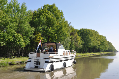 Un barco navega por un canal tranquilo rodeado de árboles en Camping Het Veen en Amberes, Bélgica.