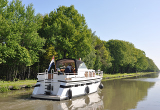 En båd sejler på en stille kanal omgivet af grønne træer ved Camping Het Veen i Antwerpen, Belgien.