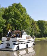 A boat cruising a calm canal lined with green trees at Camping Het Veen holiday park in Antwerp, Belgium.