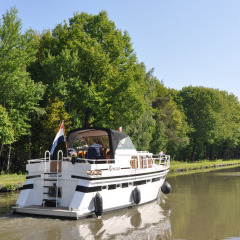 Un barco navega por un canal tranquilo rodeado de árboles en Camping Het Veen en Amberes, Bélgica.