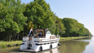 Un barco navega por un canal tranquilo rodeado de árboles en Camping Het Veen en Amberes, Bélgica.