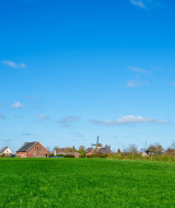 Paisaje en las cercanías de Winterswijk-Meddo, Gelderland, Países Bajos, con campos verdes y casas bajo cielo azul.