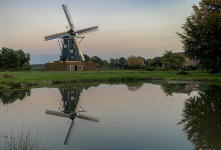 Molino de viento y campos tranquilos cerca de Winterswijk-Meddo, Gelderland, Países Bajos, reflejados en un estanque sereno al atardecer.