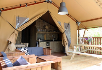 Safari tent met houten meubels, picknicktafel, open ingang en een keukenruimte achterin.