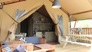 Safari tent met houten meubels, picknicktafel, open ingang en een keukenruimte achterin.