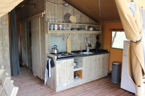 Area cucina in una tenda safari al Lac du Causse, Francia, con arredamento in legno e fornelli.