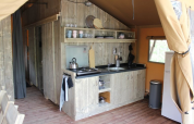 Zona de cocina dentro de una tienda safari en Lac du Causse, Francia, con decoración rústica y electrodomésticos.