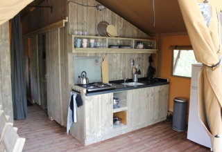 Zona de cocina dentro de una tienda safari en Lac du Causse, Francia, con decoración rústica y electrodomésticos.