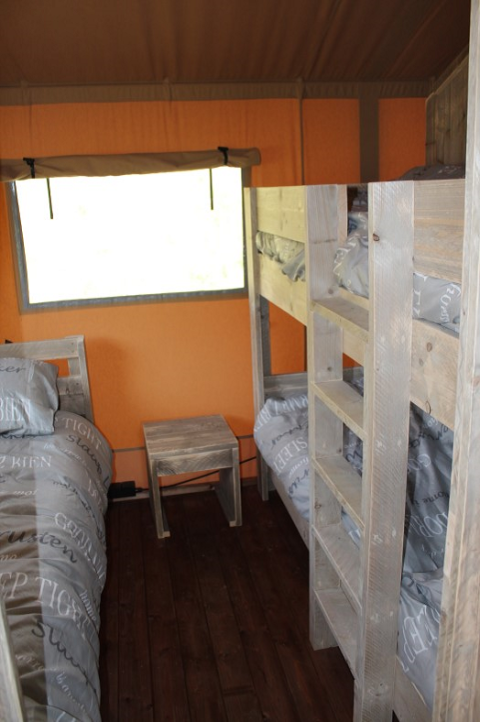 Vista interior del área de dormir con literas y muebles de madera en una tienda safari en Lac du Causse, Francia.