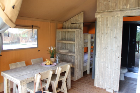 Interior de una tienda safari en Lac du Causse, Francia, con mesa de comedor, literas y baño visibles.