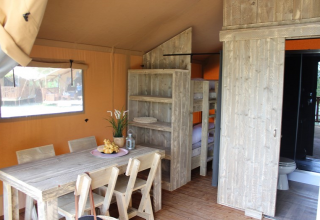 Interior de una tienda safari en Lac du Causse, Francia, con mesa de comedor, literas y baño visibles.