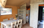 Interior de una tienda safari en Lac du Causse, Francia, con mesa de comedor, literas y baño visibles.