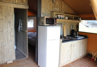 Vista interior de cocina y dormitorio en una tienda safari en Lac du Causse, Francia, con muebles de madera.