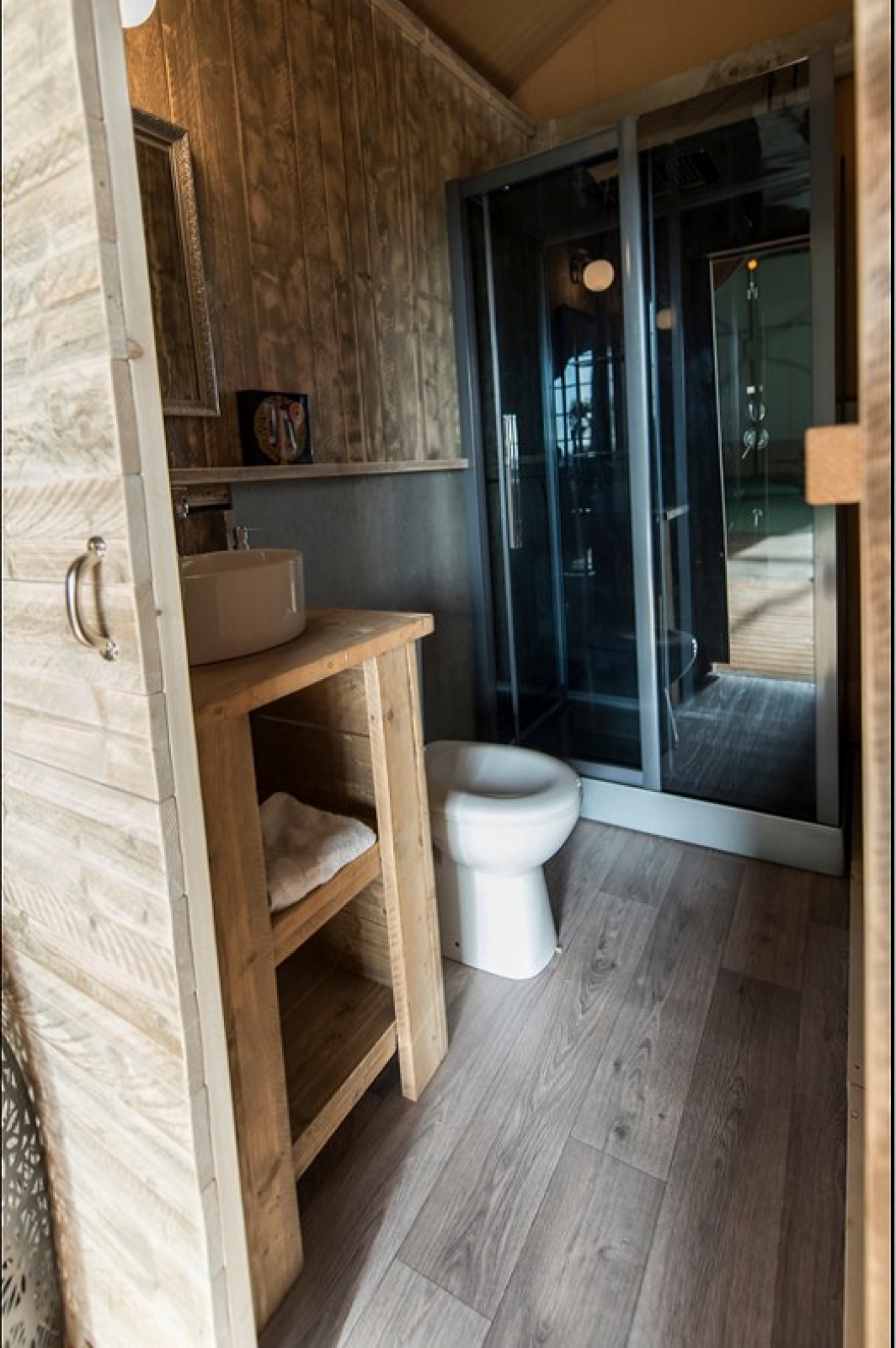 Badkamer in een safaritent bij Lac du Causse, Frankrijk, met houten meubels, wasbak, toilet en douche.