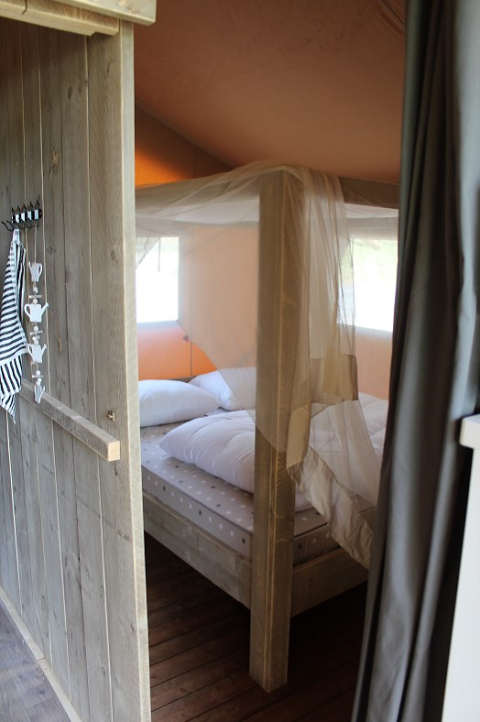 Acogedor dormitorio con cama con dosel y mosquitera en una tienda safari en Lac du Causse, Francia.