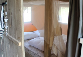 Knusse slaapkamer met hemelbed en klamboe in een safaritent bij Lac du Causse, Frankrijk.