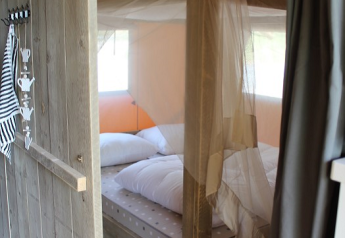 Acogedor dormitorio con cama con dosel y mosquitera en una tienda safari en Lac du Causse, Francia.