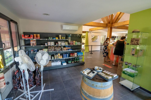 Interior de tienda en Lac du Causse, parque vacacional en Nouvelle-Aquitaine, Francia, con estantes y clientes.