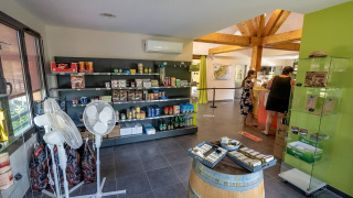Interior de tienda en Lac du Causse, parque vacacional en Nouvelle-Aquitaine, Francia, con estantes y clientes.