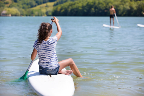 En person sidder på et paddleboard i Lac du Causse, Nouvelle-Aquitaine, Frankrig, på en solrig dag.