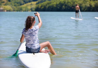 Persona seduta su una tavola da paddle al Lac du Causse, Nouvelle-Aquitaine, Francia, in una giornata di sole.
