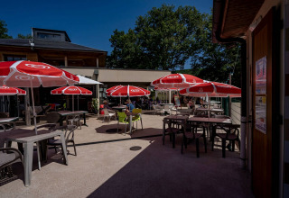 Outdoor terrace with red umbrellas and tables at Lac du Causse holiday park in Nouvelle-Aquitaine, France.