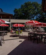 Terraza exterior con sombrillas rojas y mesas en Lac du Causse, parque vacacional en Nouvelle-Aquitaine, Francia.