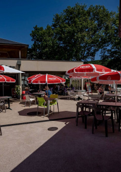 Terraza exterior con sombrillas rojas y mesas en Lac du Causse, parque vacacional en Nouvelle-Aquitaine, Francia.
