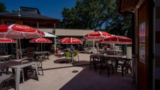 Terraza exterior con sombrillas rojas y mesas en Lac du Causse, parque vacacional en Nouvelle-Aquitaine, Francia.