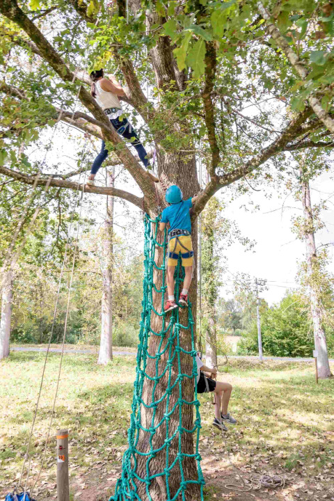Niños subiendo una red de cuerda en un árbol en el parque vacacional Lac du Causse, Nouvelle-Aquitaine, Francia.