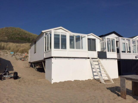Strandhuis 'Dishoek 345/346' met witte buitenkant en glasveranda, geplaatst op zand bij een rijdende duin.